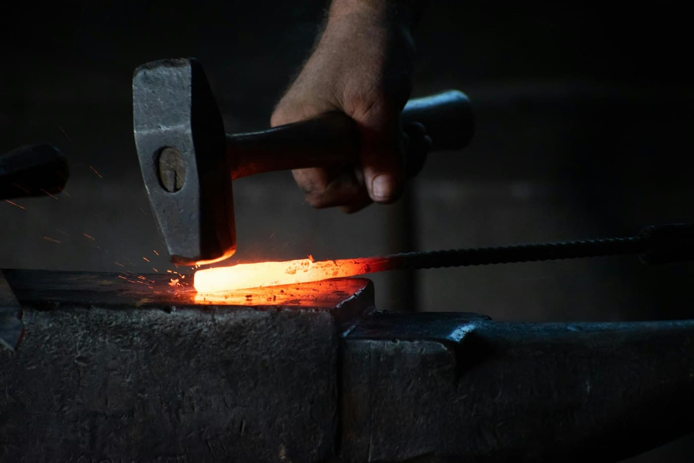 Un martillo golpeando una barra de hierro al rojo sobre un yunque
